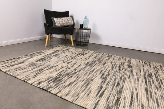 Large wool rug with ivory and charcoal woven stripe pattern, angled view