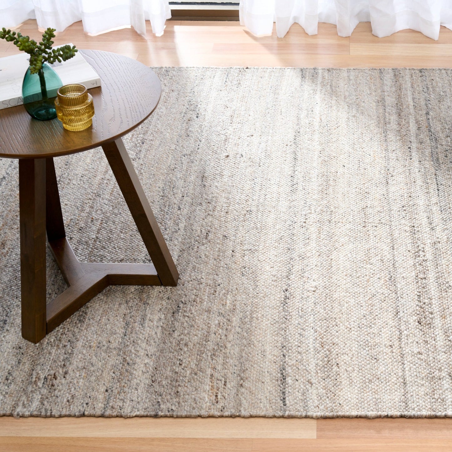 Dark grey wool rug spread across floor near seating area, showing striped texture