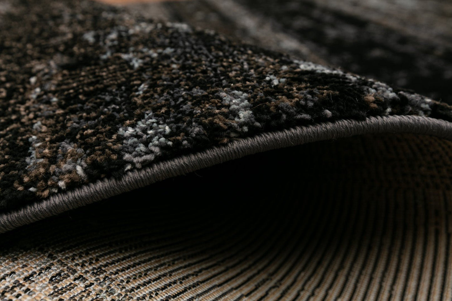 Black area rug edge with stitched binding and textured low-pile surface