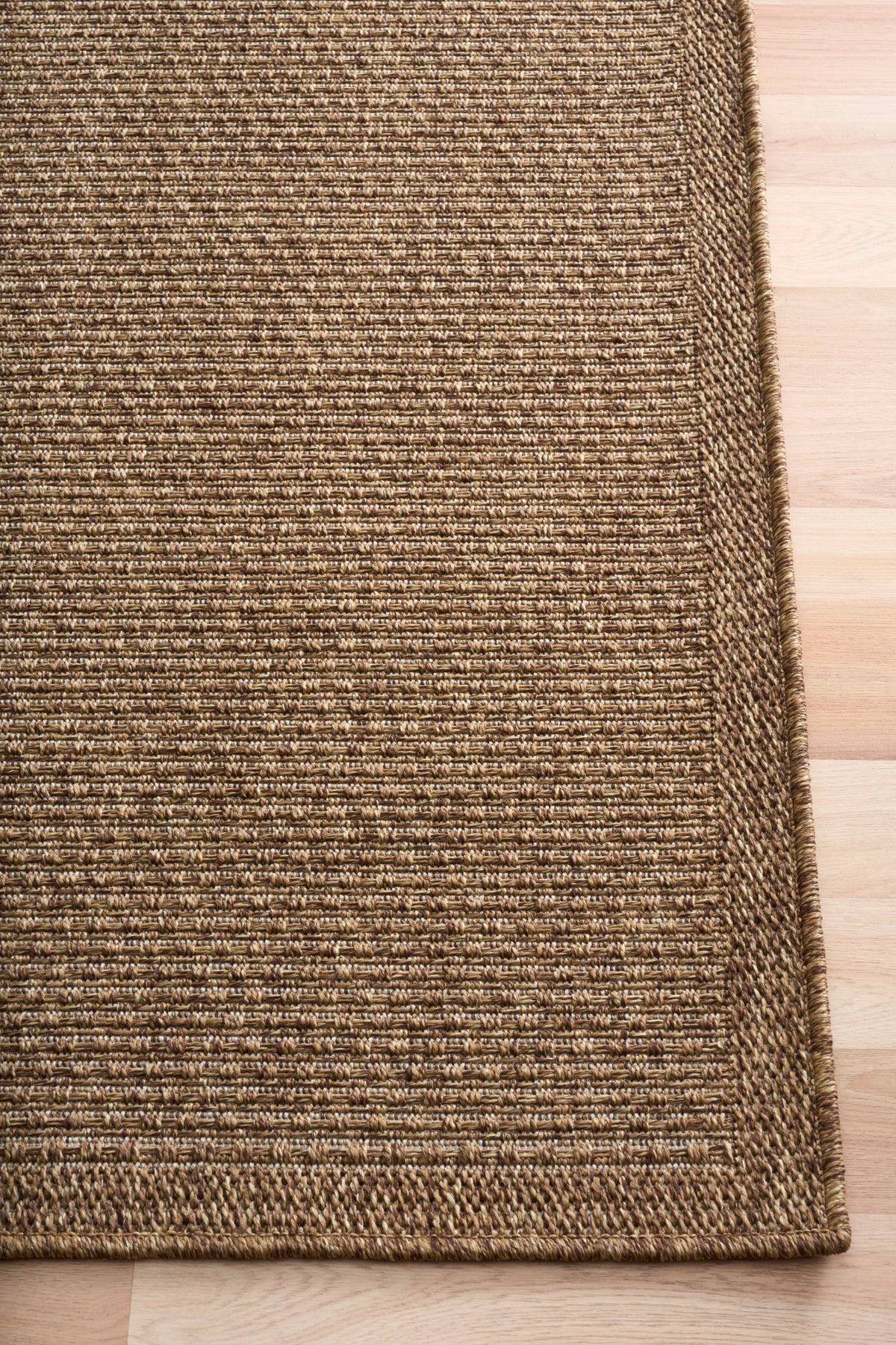 Close-up of rug border and corner with tan-brown woven texture on wood flooring