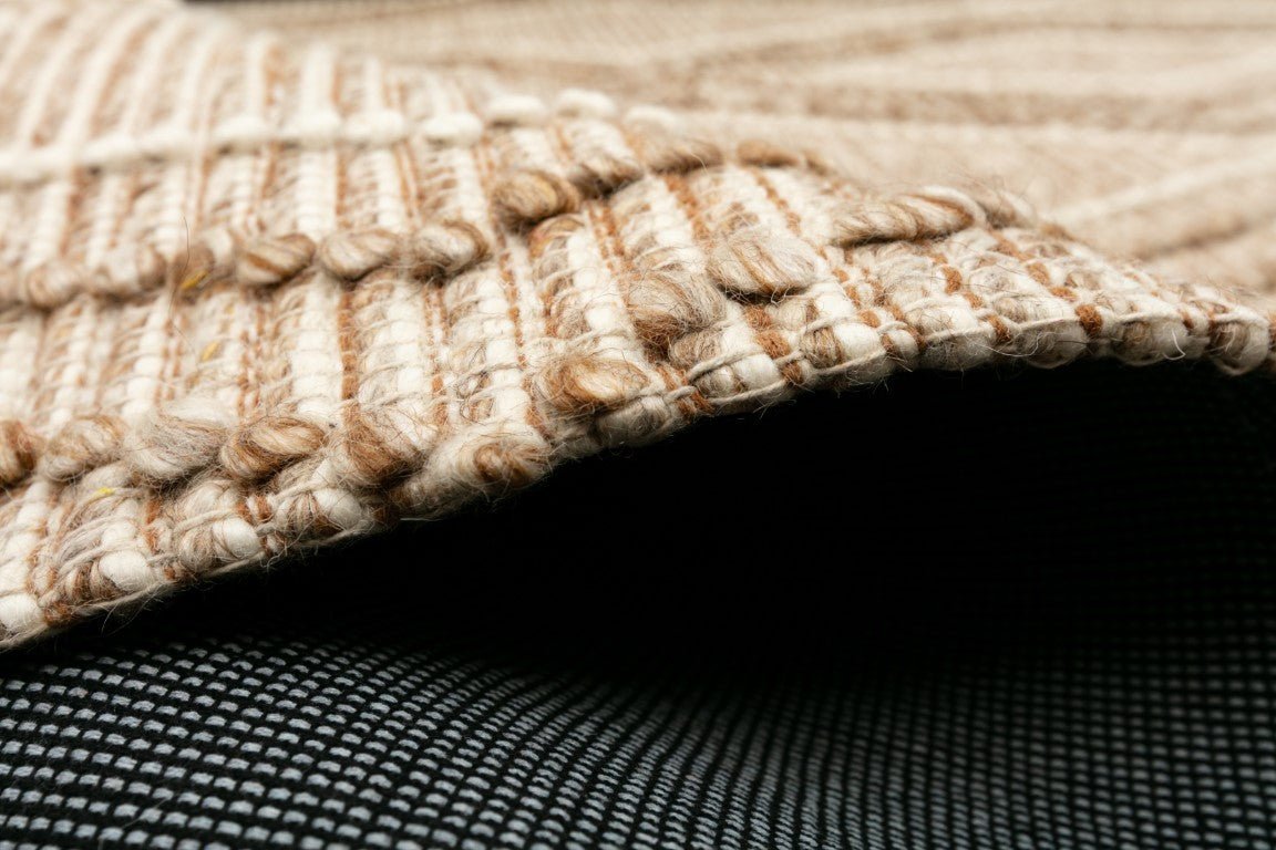 Beige wool rug corner with braided edge and dark underside backing