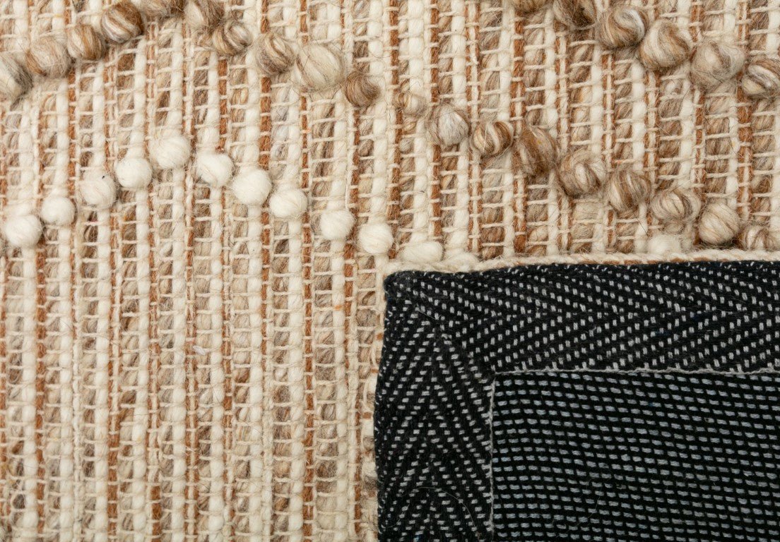 Beige wool area rug border close-up with stitched woven pattern and black backing