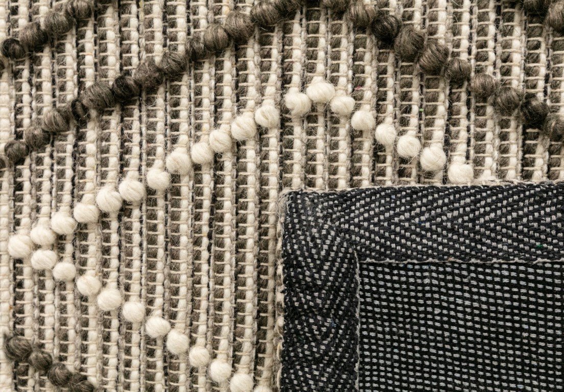 Close-up of wool rug edge with pom fringe and charcoal woven trim.