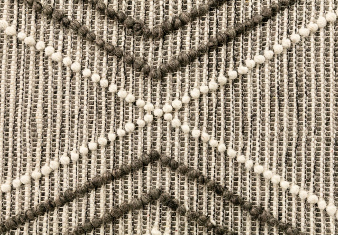 Woven wool rug detail with raised lattice texture and cream pom fringe accents.