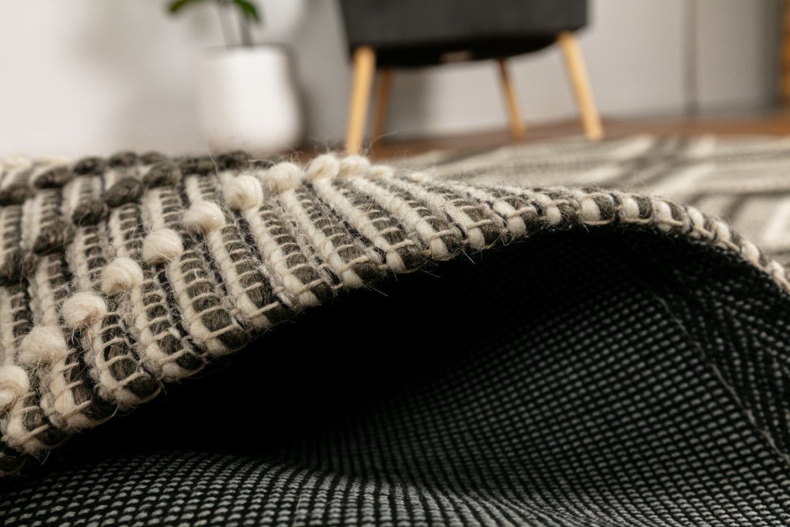 Rolled corner detail of charcoal and cream wool rug with textured weave and binding.