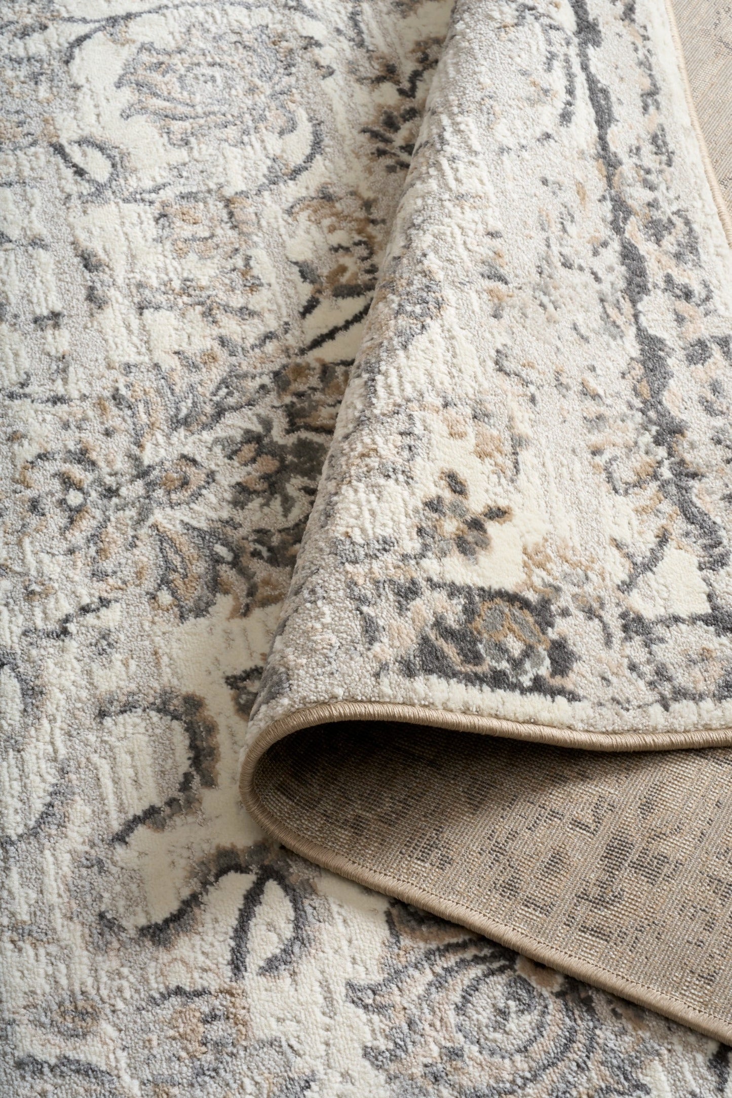Grey and cream damask area rug with textured backing visible along rolled edge