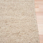 Beige woven rug corner with stitched edge and textured pile