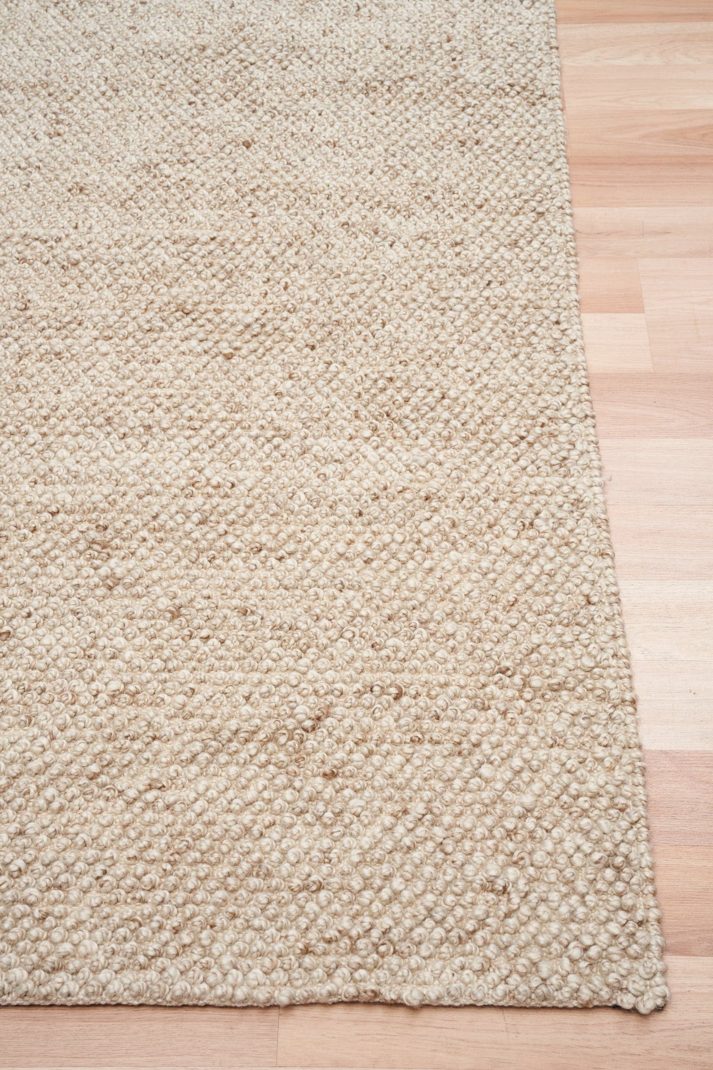 Beige woven rug corner with stitched edge and textured pile