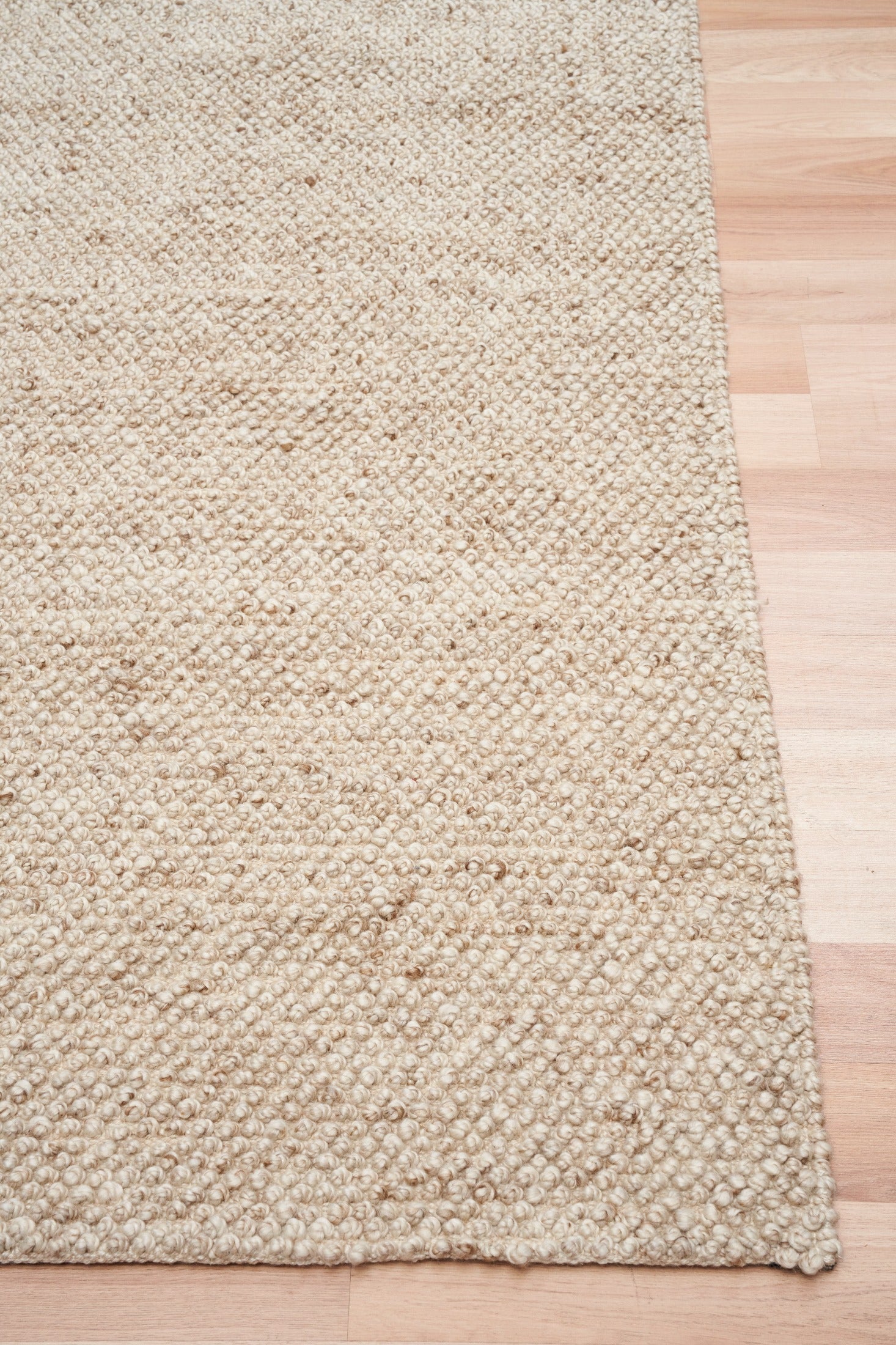Beige woven rug corner with stitched edge and textured pile
