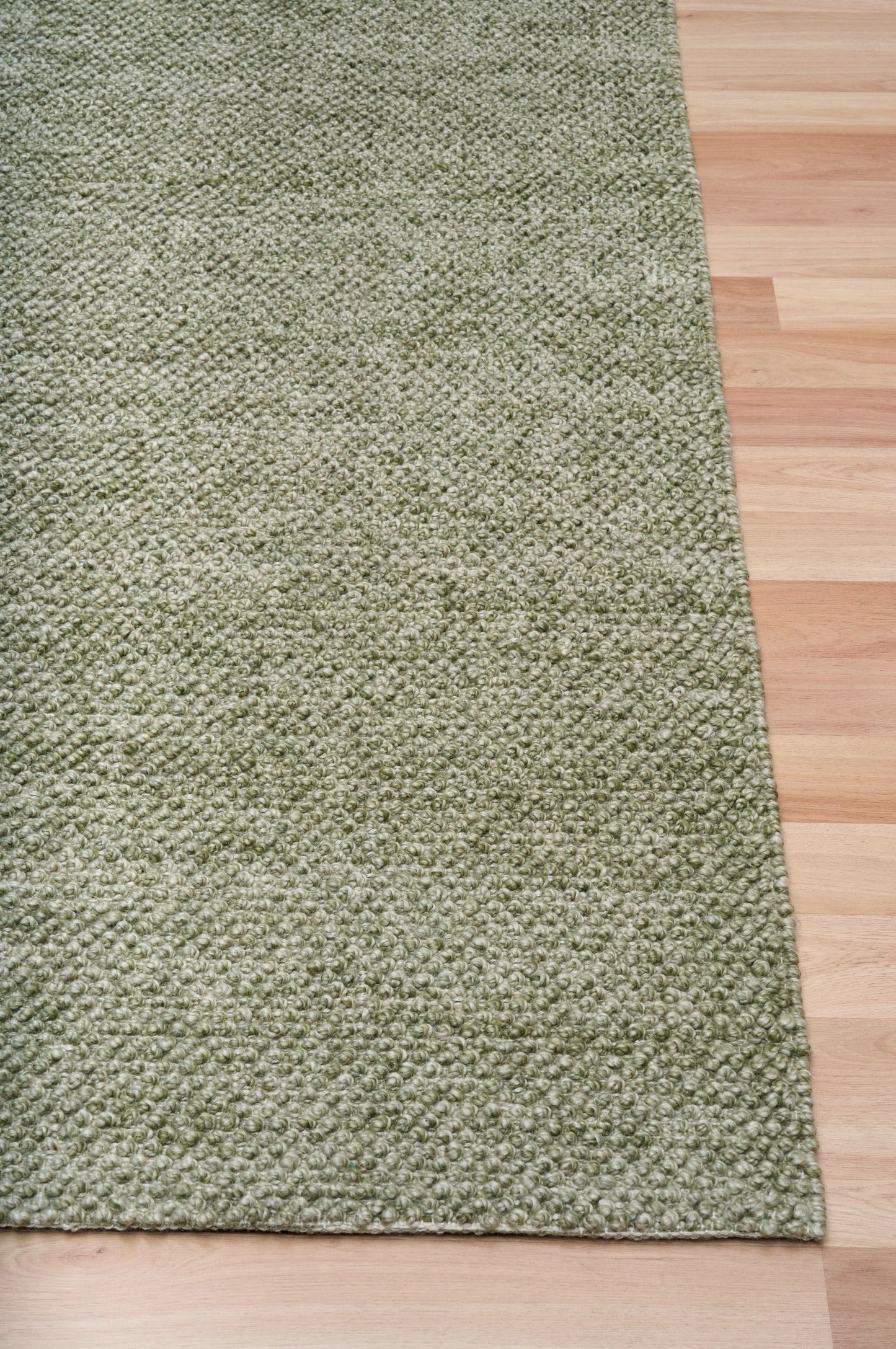 Olive green textured area rug with flat border along the corner