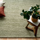 Olive green textured area rug laid on light wood flooring