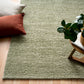 Olive green textured square area rug with visible corner and backing