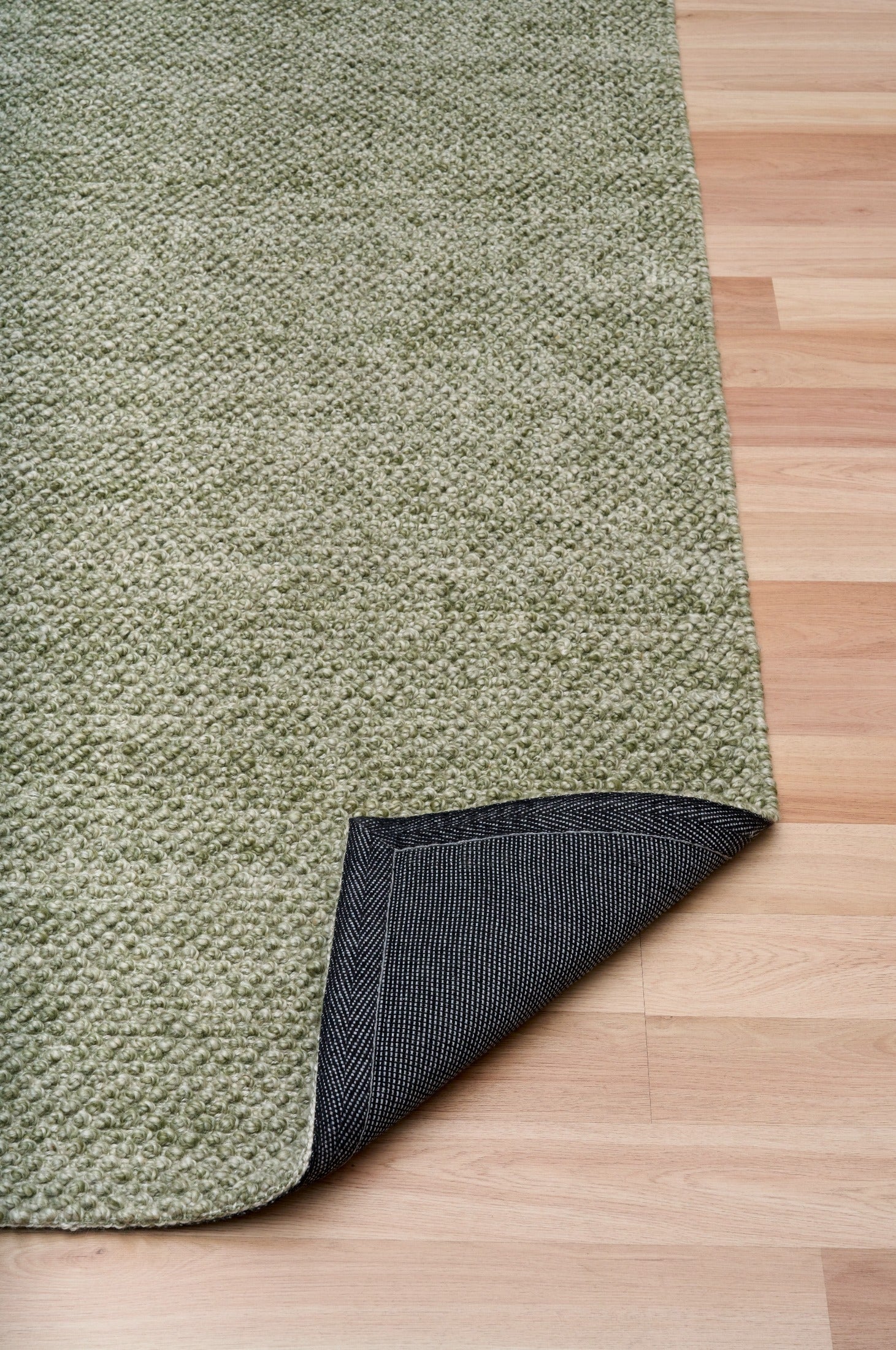 Olive green area rug with dark backing visible at folded corner