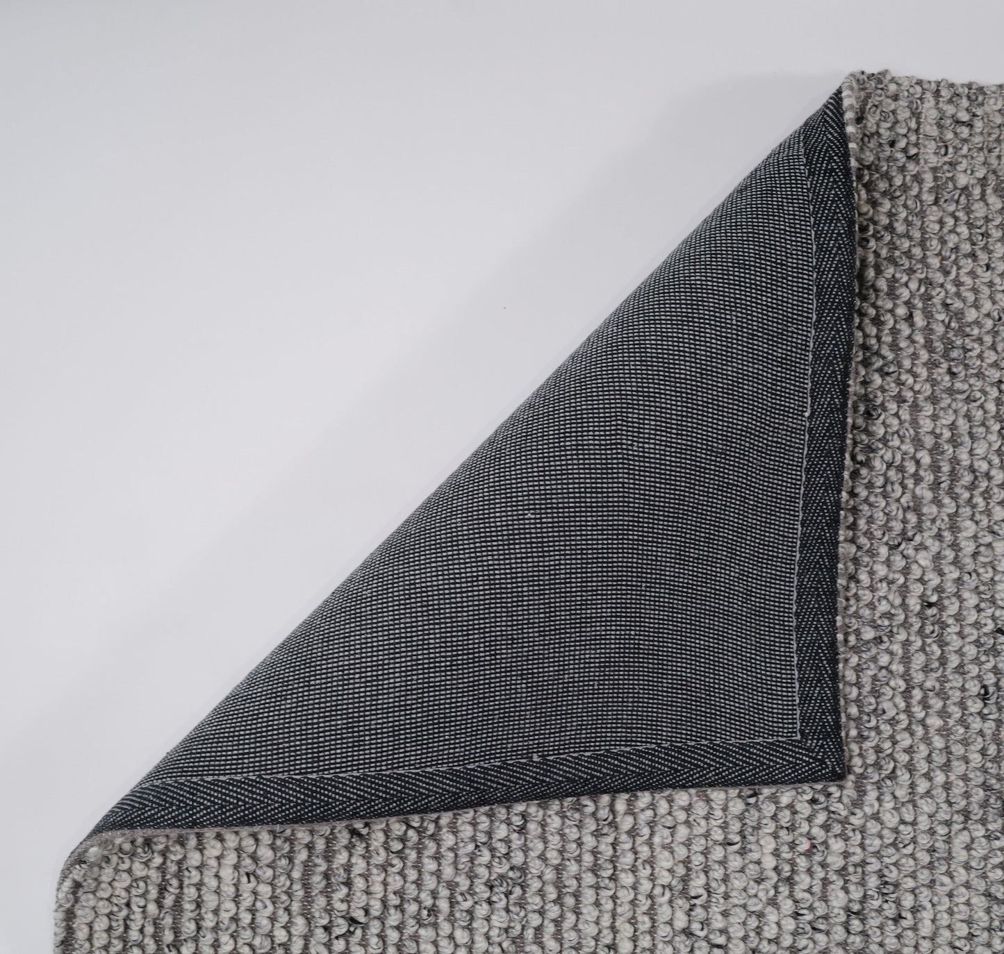 Grey textured rug edge with visible seam and overlocked binding