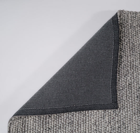 Grey textured rug edge with visible seam and overlocked binding