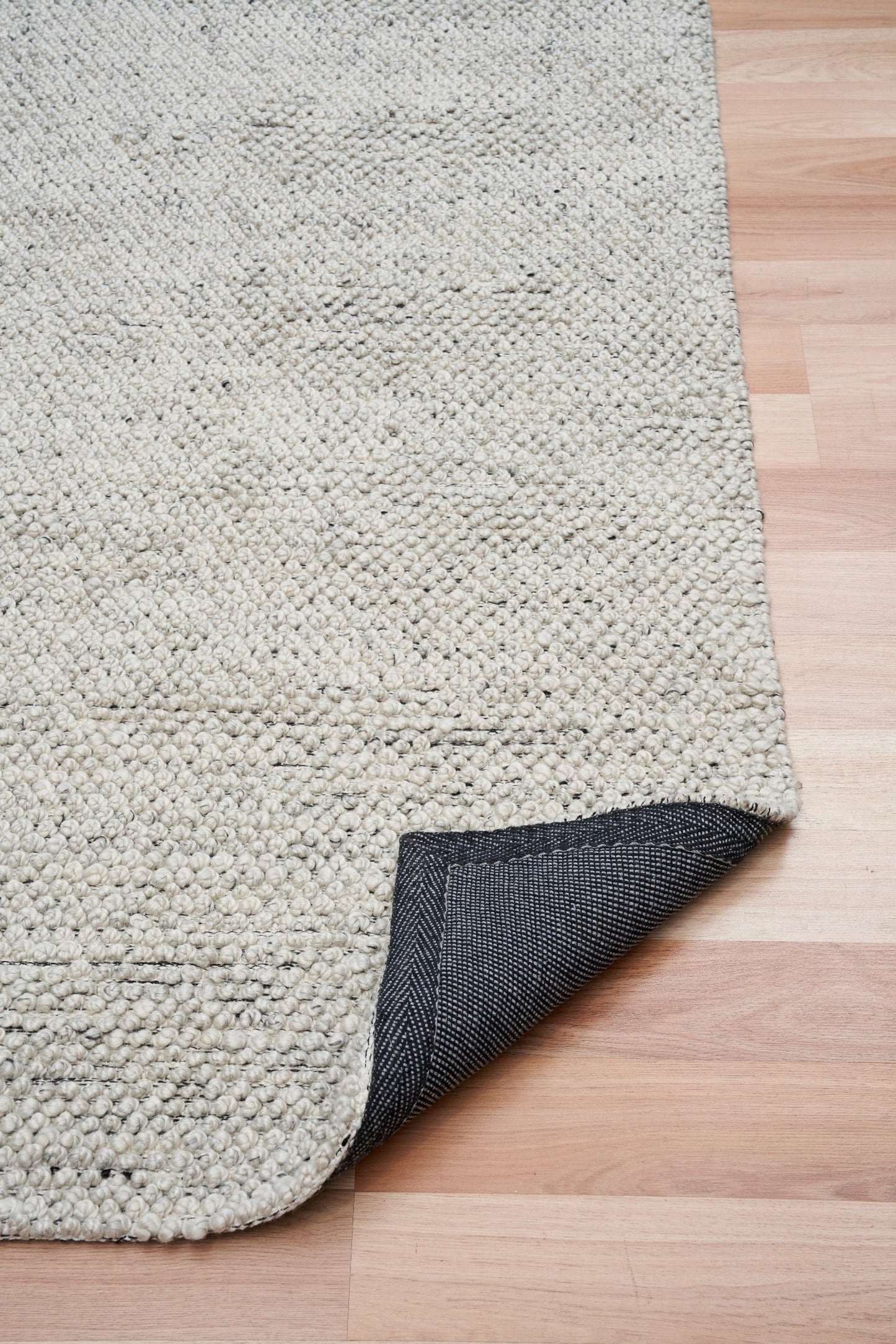 Grey textured area rug with dark backing visible at corner fold