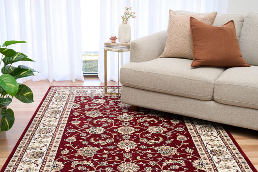 Burgundy floral area rug under a living room sofa, cream border visible