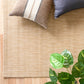 Light beige woven rug with textured weave and corner detail near pillows