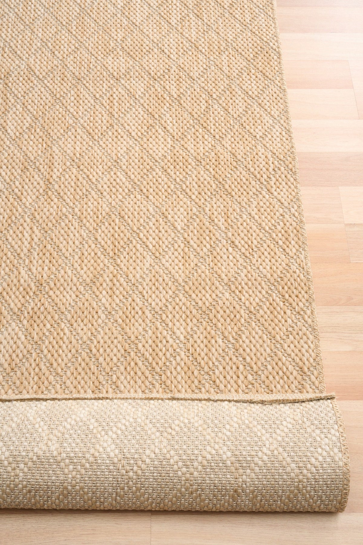 Beige woven rug corner with visible folded border and dense loop weave.