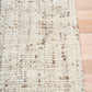 Beige textured area rug with stitched edge and mottled woven pattern