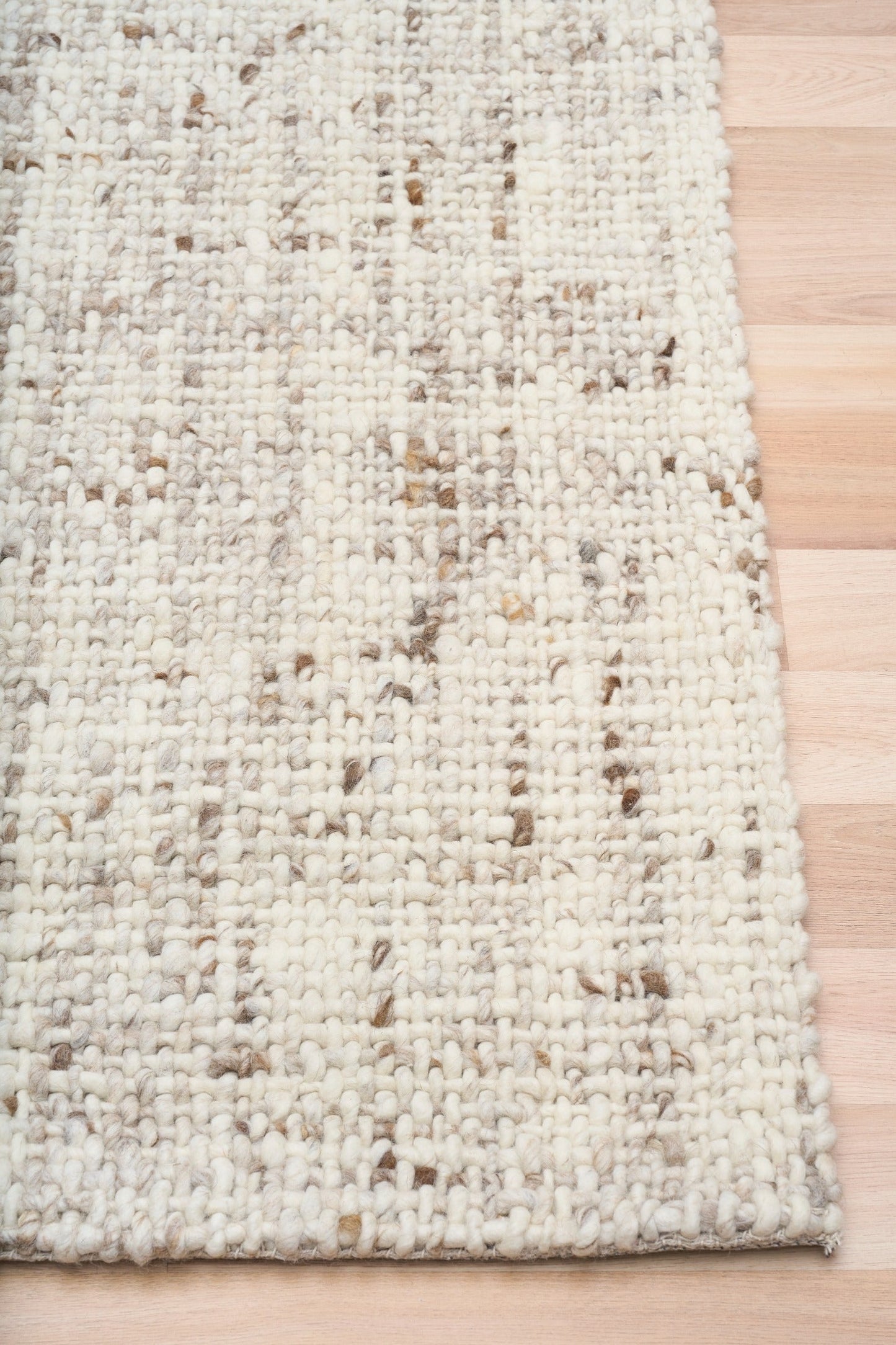 Beige textured area rug with stitched edge and mottled woven pattern