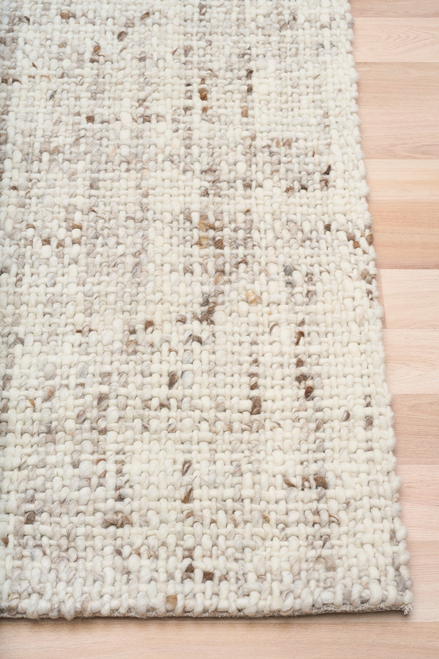 Beige textured area rug with stitched edge and mottled woven pattern