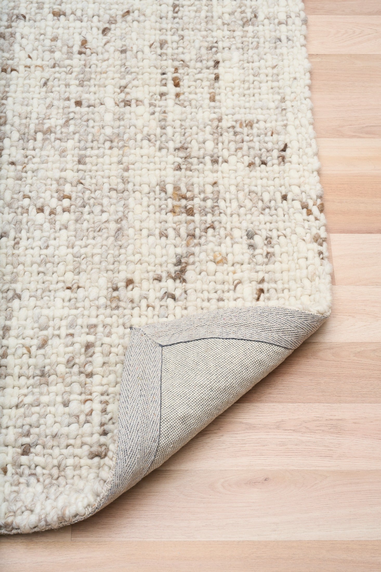 Beige textured area rug corner with visible woven backing and stitched border