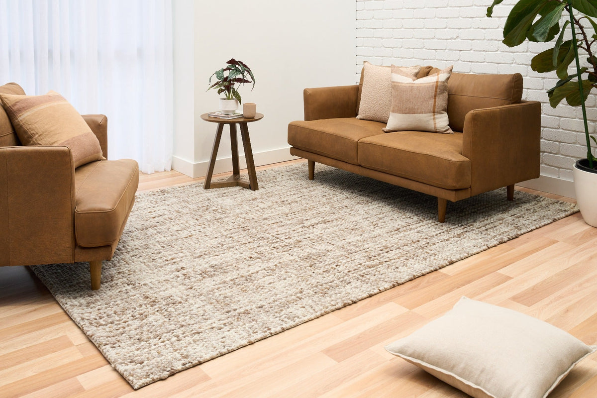 Large wool area rug on hardwood floor, beige with brown speckled texture