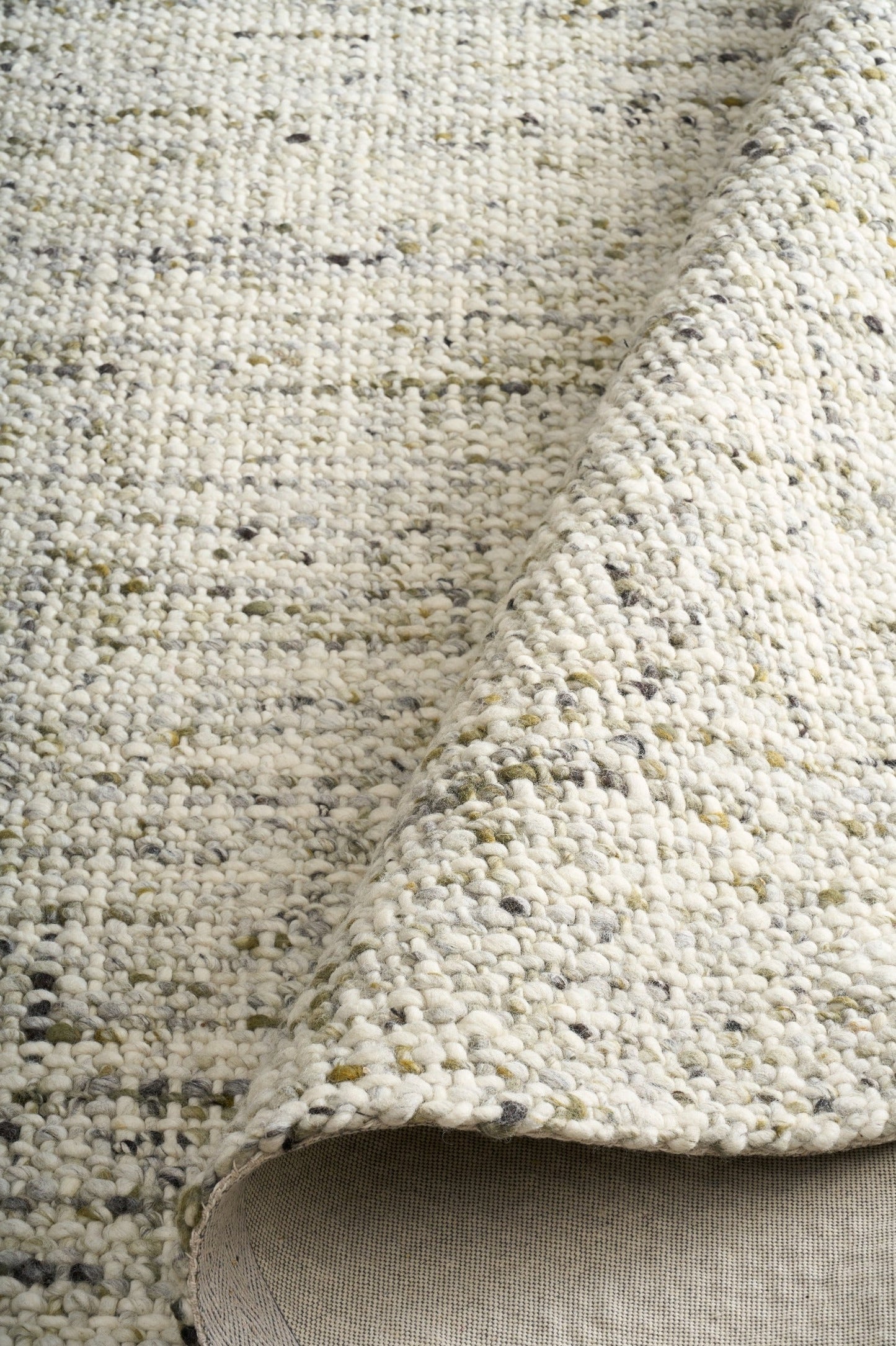 Ivory and light green textured area rug close-up with short pile and stitched edge