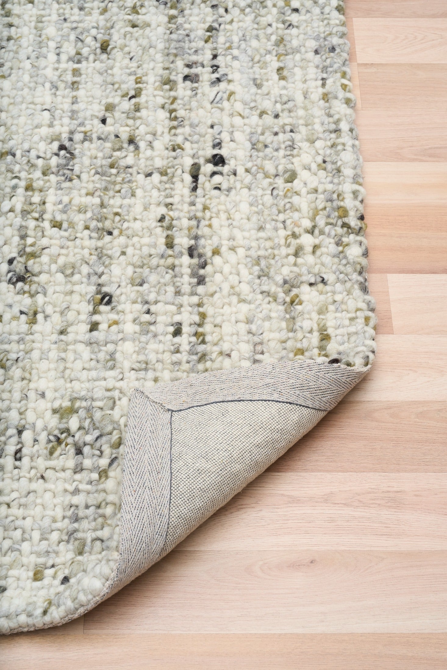 Ivory and light green textured rug corner with stitched border detail