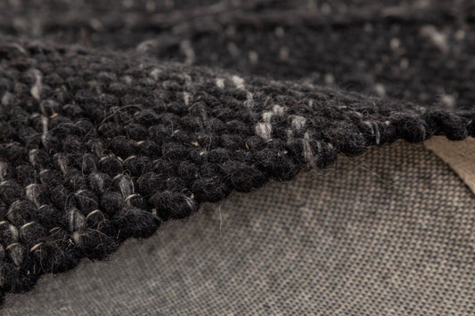 Dark wool rug with looped pile texture and beige backing edge visible