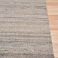 Dark grey wool rug corner view with horizontal stripes on light wood flooring