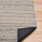 Dark grey wool rug with visible folded edge and textured backing on wood floor
