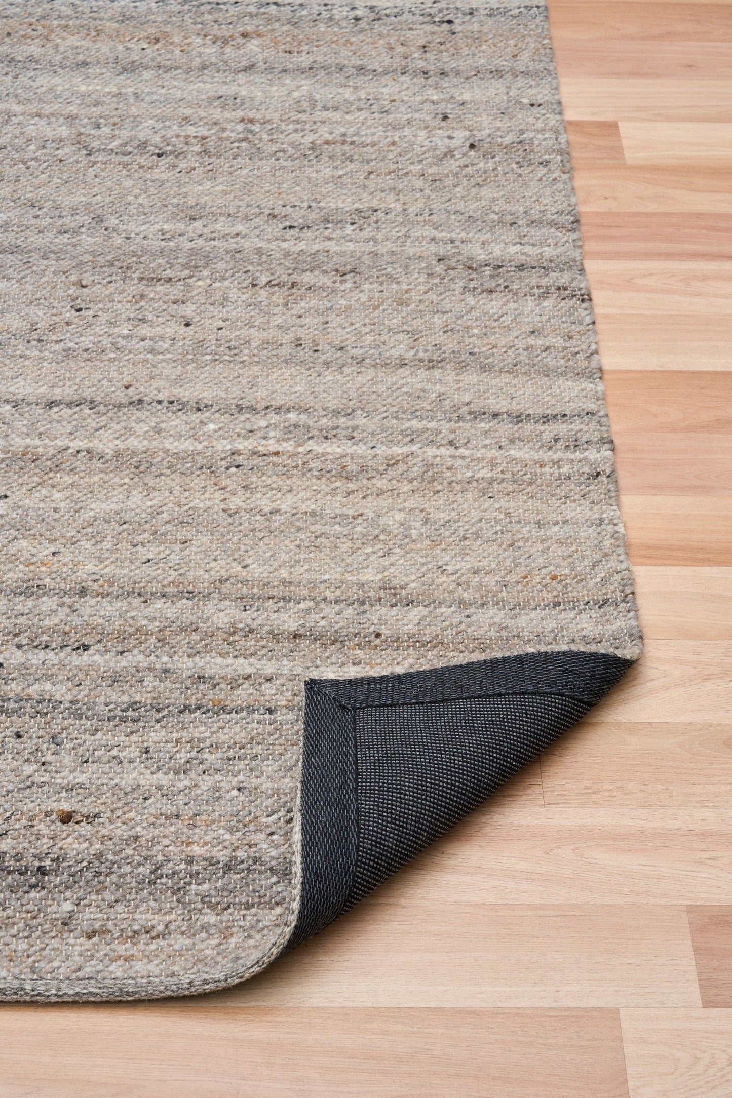 Dark grey wool rug with visible folded edge and textured backing on wood floor