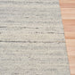 Grey wool rug corner with visible border weave and speckled texture