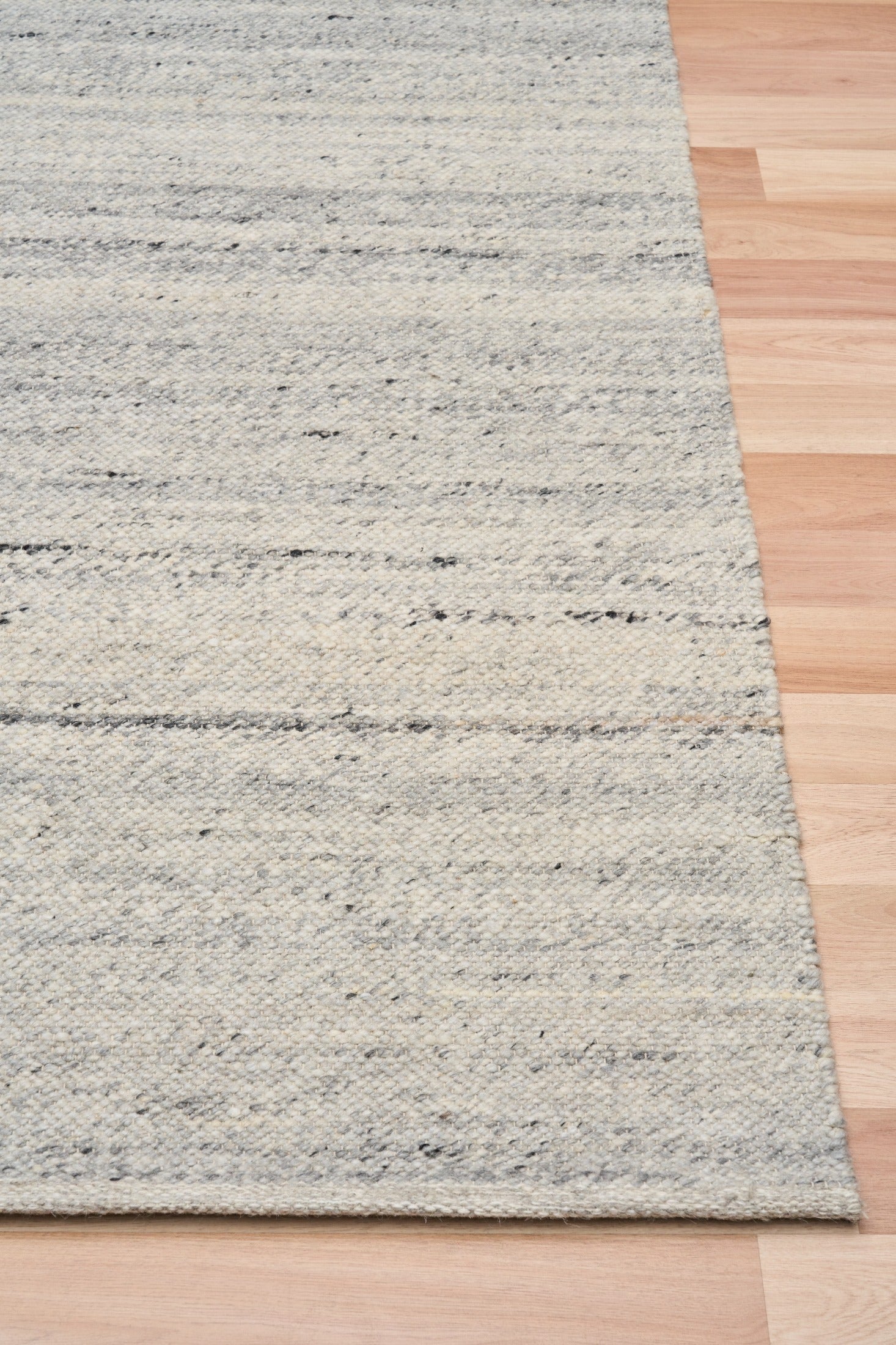 Grey wool rug corner with visible border weave and speckled texture