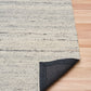Grey wool rug edge turned to show backing fabric and speckled texture