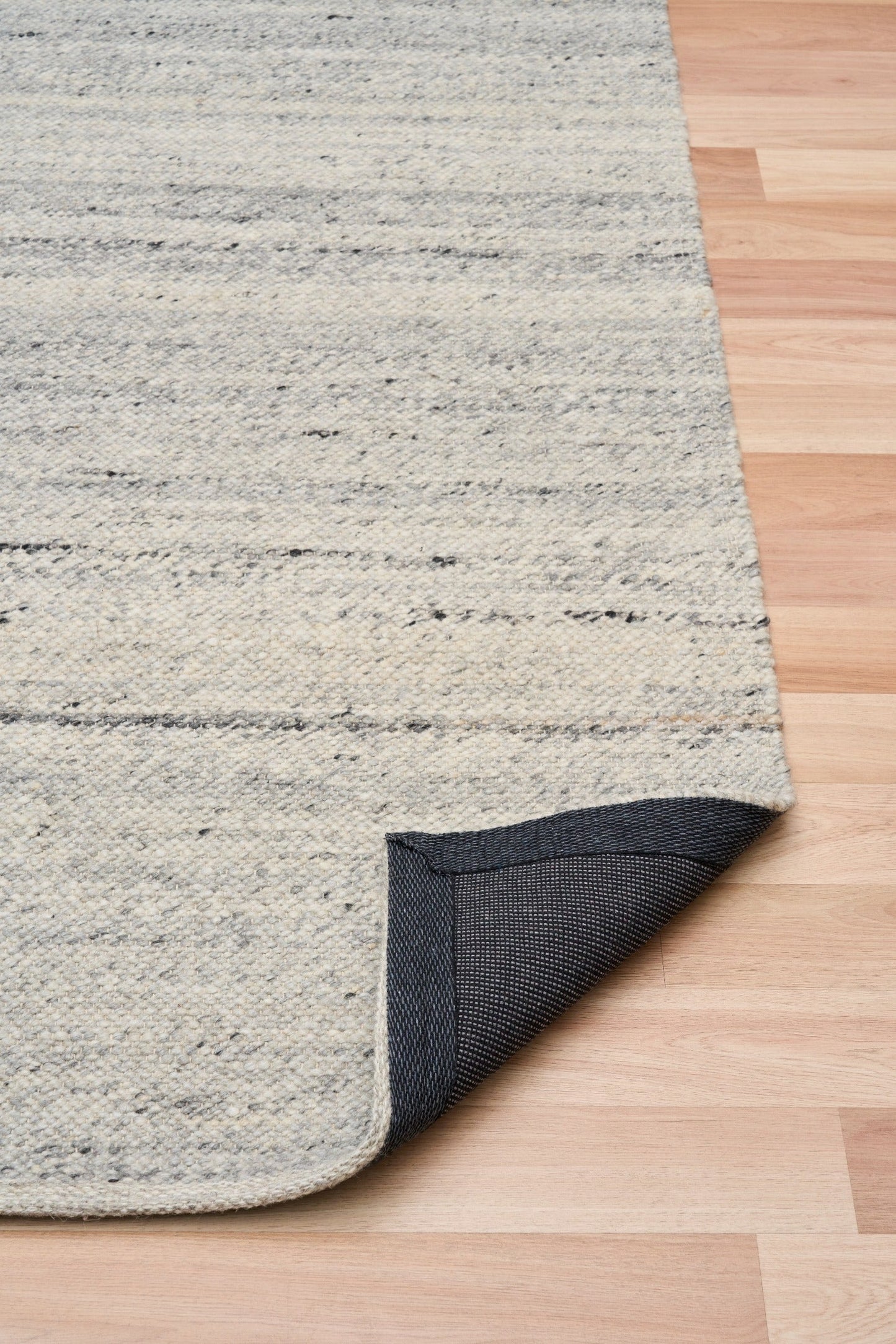 Grey wool rug edge turned to show backing fabric and speckled texture