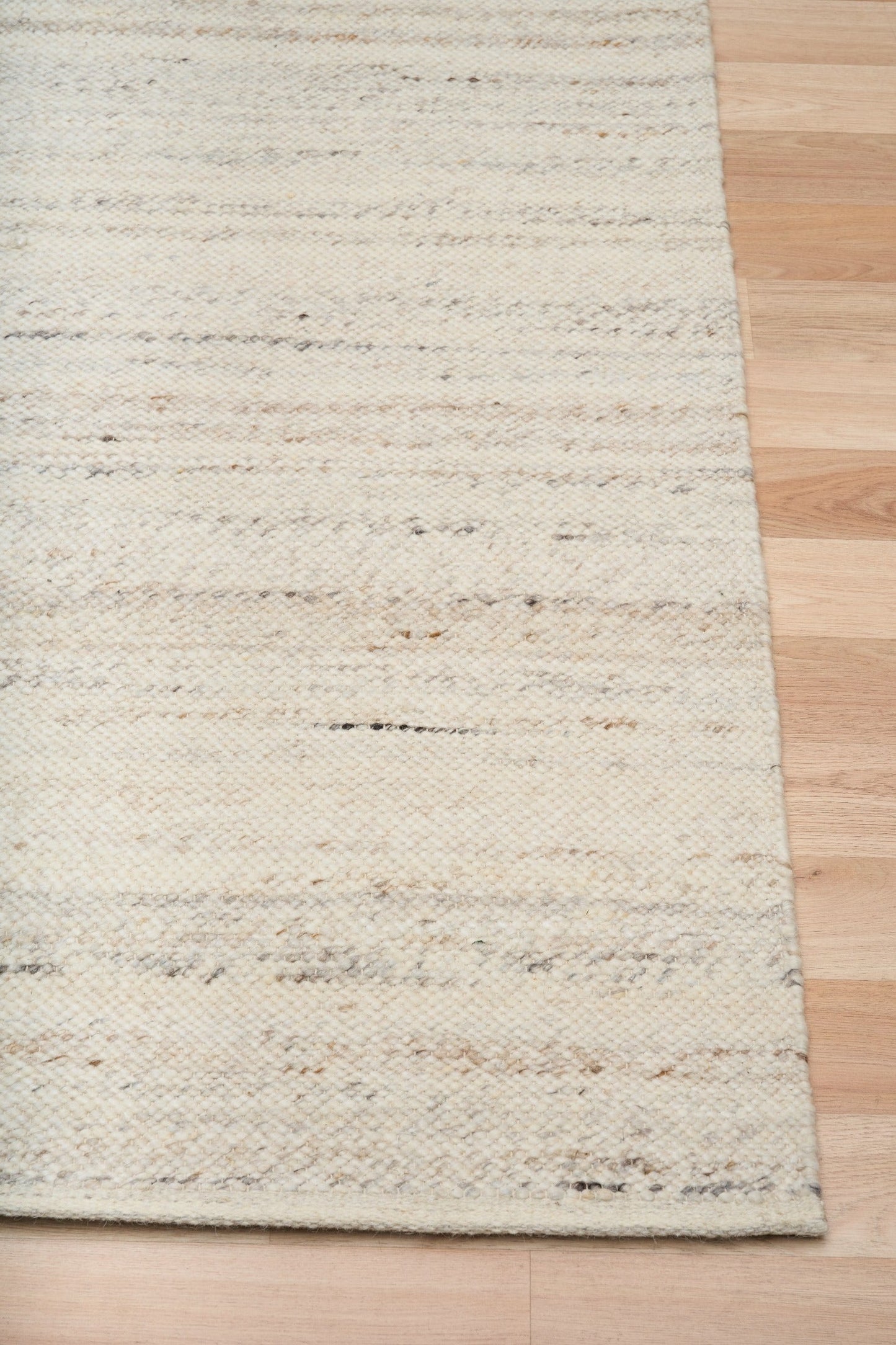 White wool rug corner with textured surface and clean overlocked edge