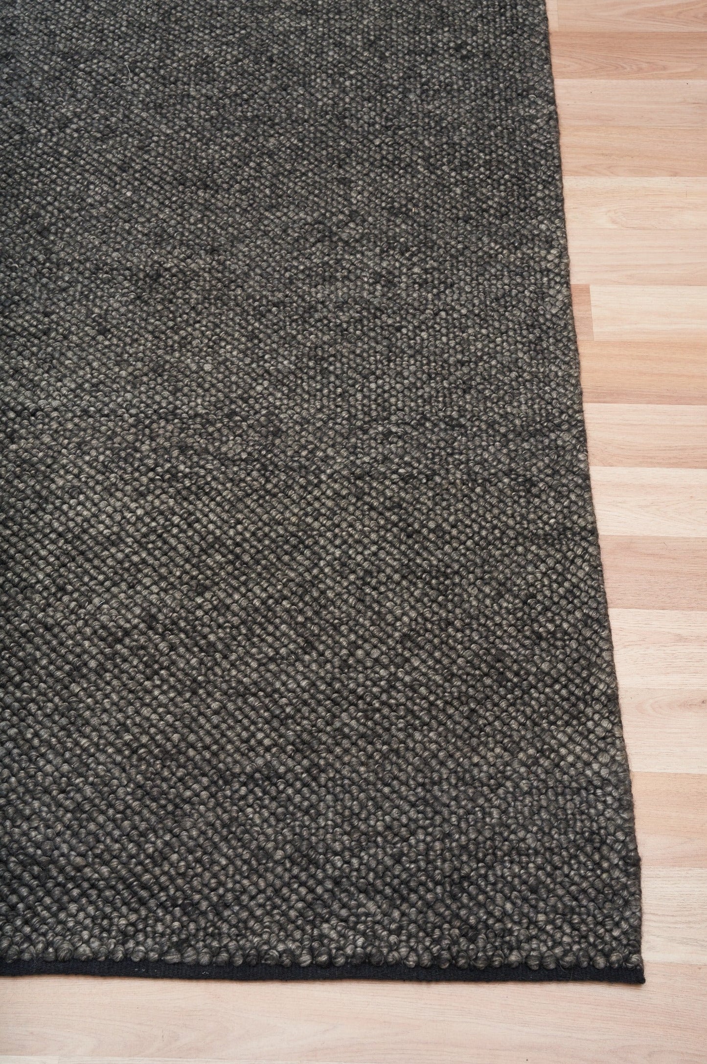 Charcoal textured area rug corner with stitched border