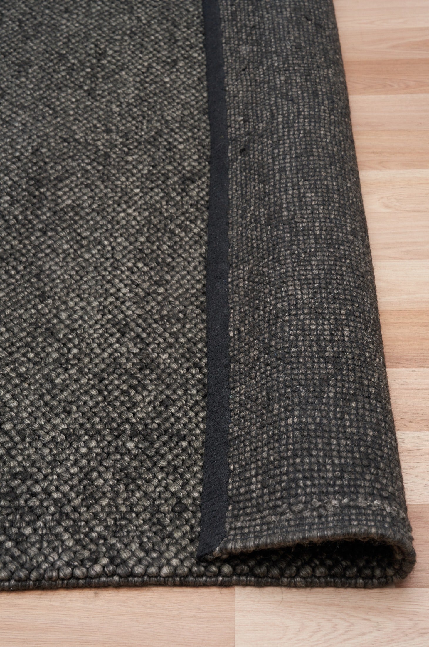 Charcoal textured area rug corner detail with thick edge binding