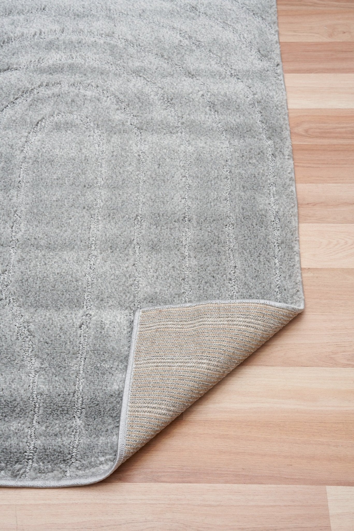 Light grey shag rug showing woven backing and stitched edge on hardwood floor