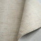 Light gray woven area rug corner showing stitched fold and underside