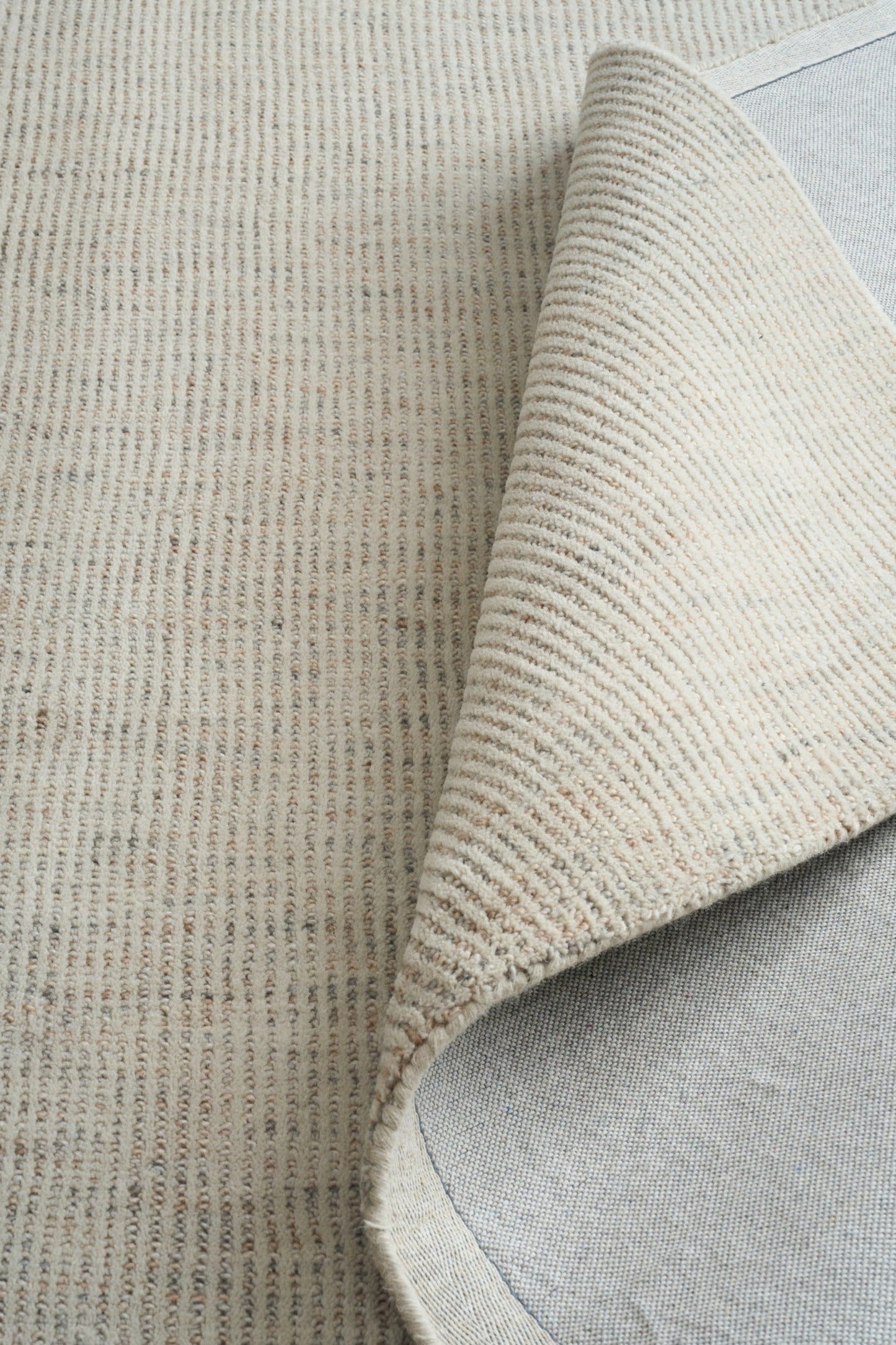 Light gray woven area rug corner showing stitched fold and underside