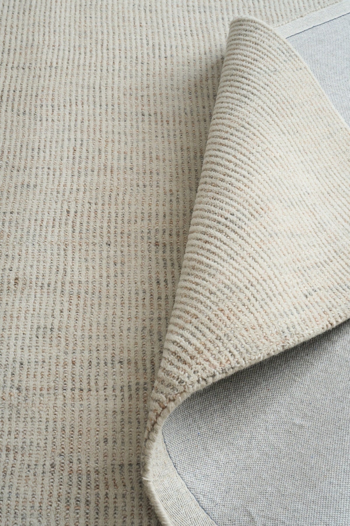 Light gray woven area rug corner showing stitched fold and underside