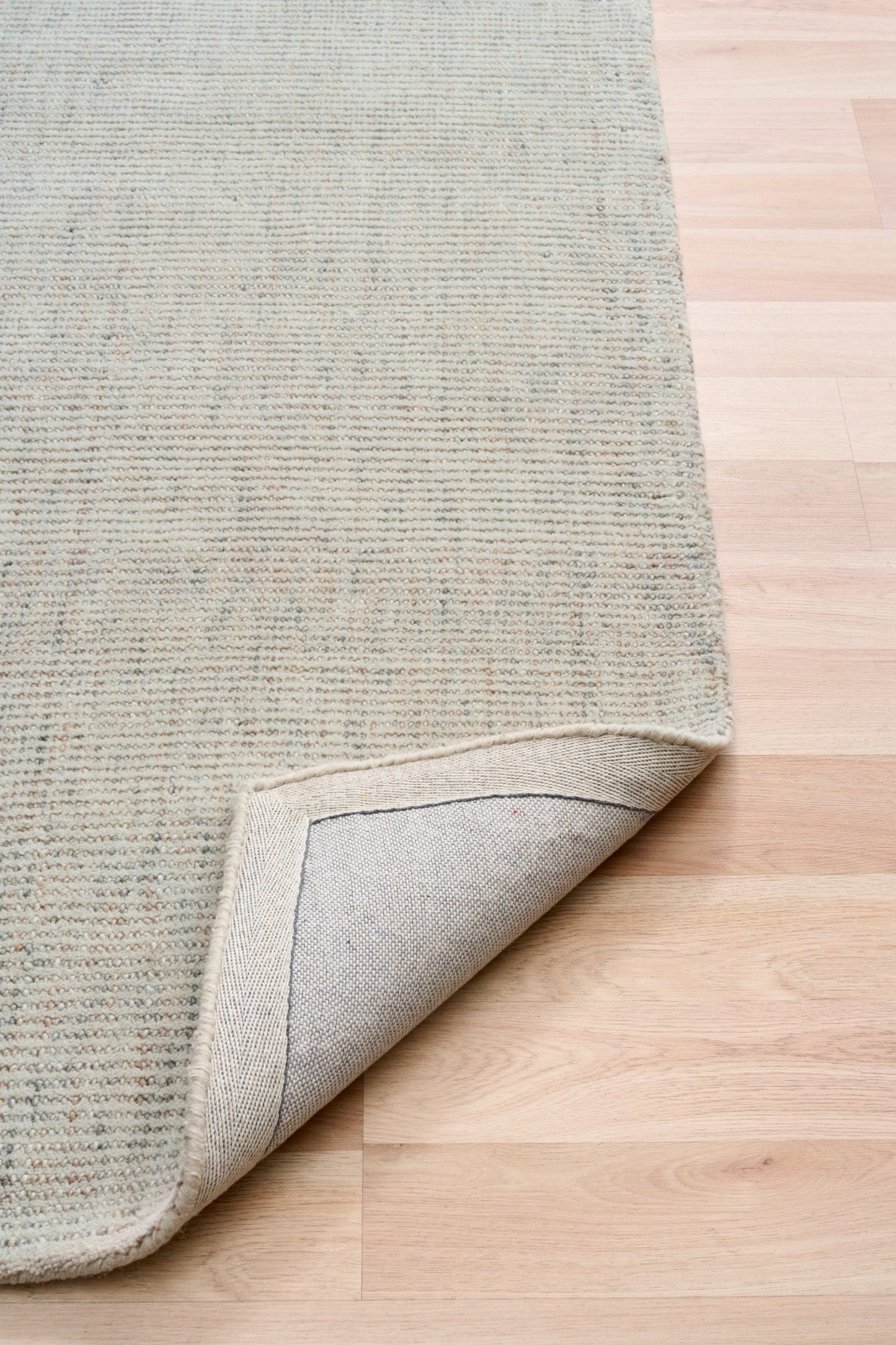 Light gray woven area rug with bound edge corner detail