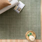 Green area rug corner with folded blankets and small wooden bowl decor, top-down
