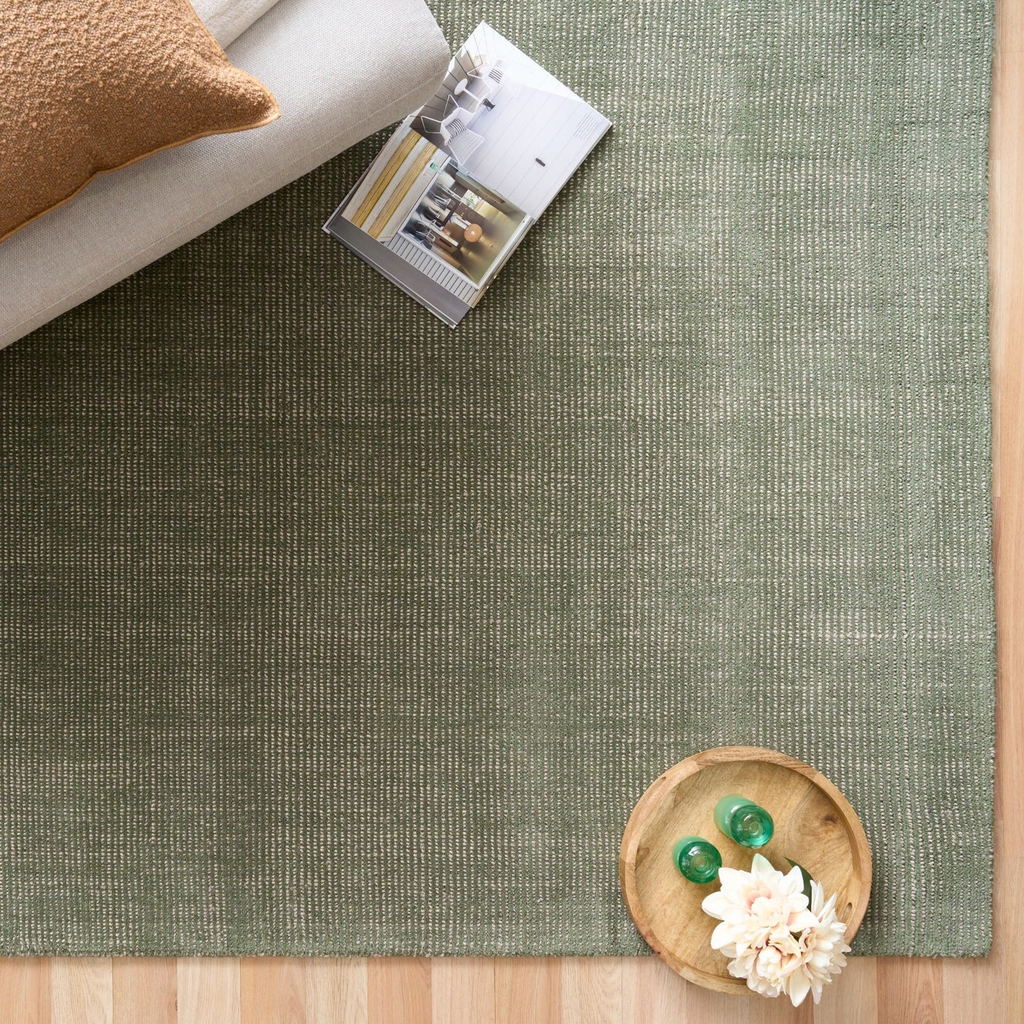 Green area rug corner with folded blankets and small wooden bowl decor, top-down