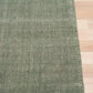 Green area rug with visible hemmed edge on light wood flooring