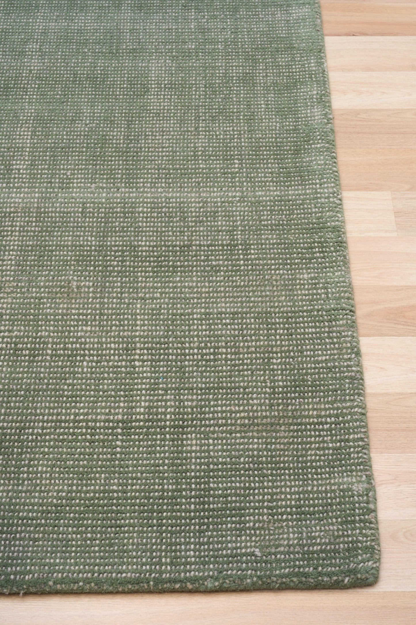 Green area rug with visible hemmed edge on light wood flooring